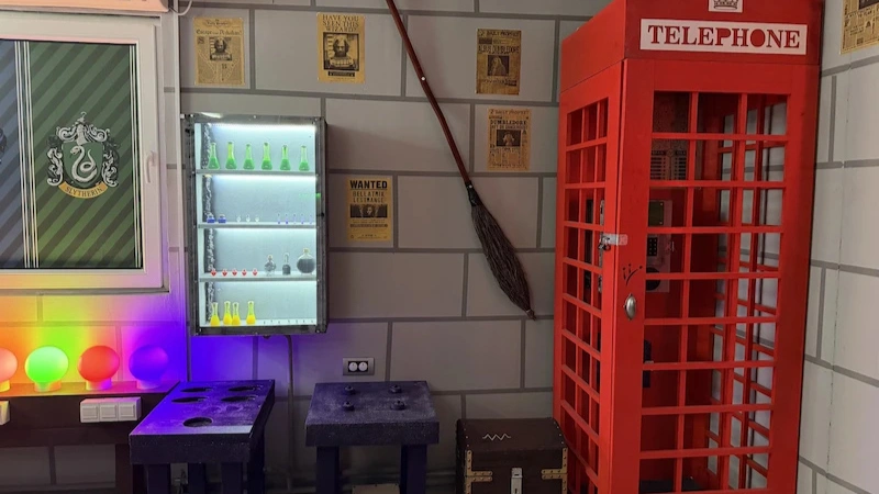 Crvena telefonska govornica, metla na zidu, crni ormar i mađioničarski rekviziti.