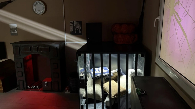 Drveni kavez sa jastucima, kamin sa crvenim osvetljenjem, paukova mreža na prozoru i zidni sat.