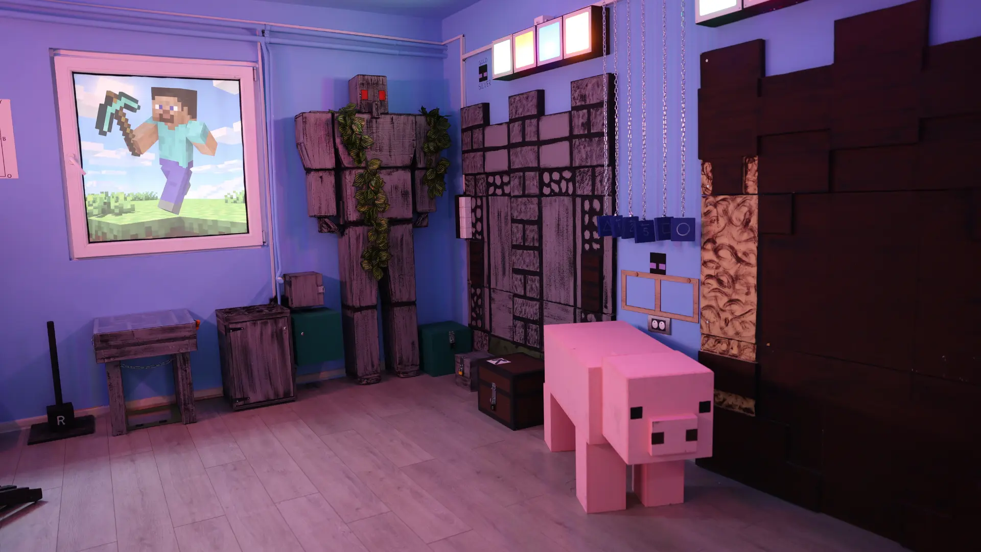 Unutrašnjost Majnkraft escape room sobe sa kockastom ružičastom svinjom, figurom gvozdenog golema, prikazom Stiva sa pijukom i zidovima uređenim u stilu Minecraft blokova.