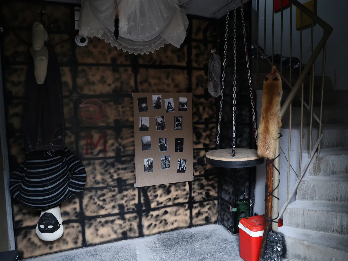 Resident Evil escape room sa stepeništem, maskiranom lutkom koja visi naglavačke i crno-belim fotografijama